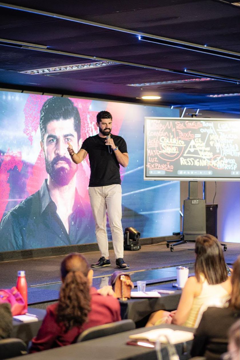 Cícero Alves no palco do Comunique-se com Impacto, com o microfone, diante da plateia